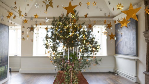 A decorated Christmas tree in a white room hung with gold stars